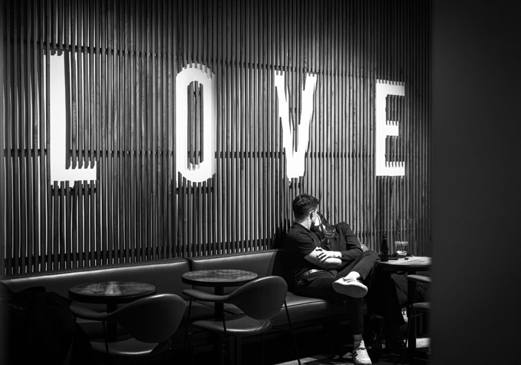 A couple that is throning dating shares an intimate moment in a café, sitting close together under a bold "LOVE" sign on a wooden-panel wall – Duo Desire.