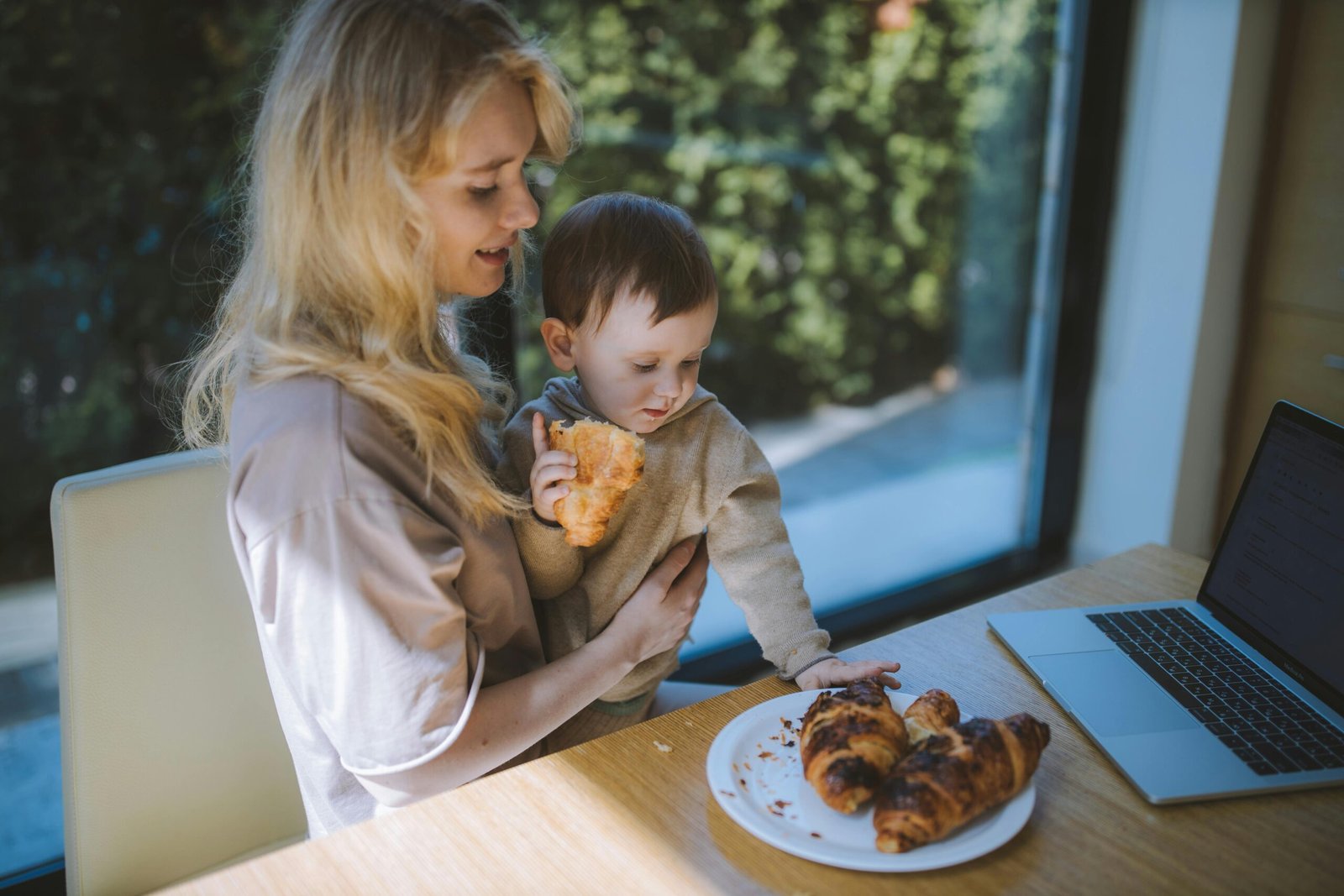 Mom and toddler sharing croissants by laptop, sweet Duo Desire breakfast moment.
