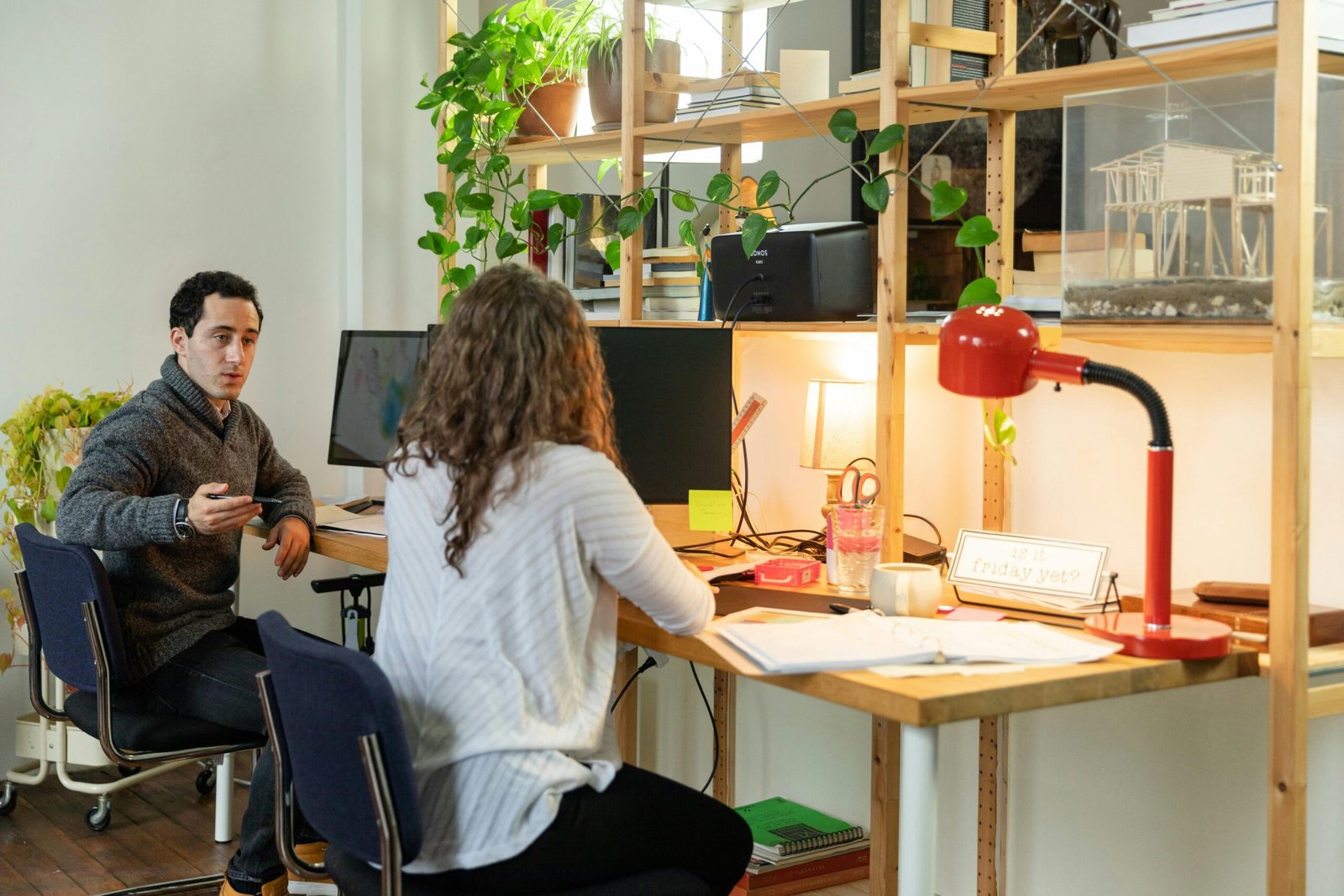 Two coworkers talking at shared desk, discussing work relationship – Duo Desire style.
