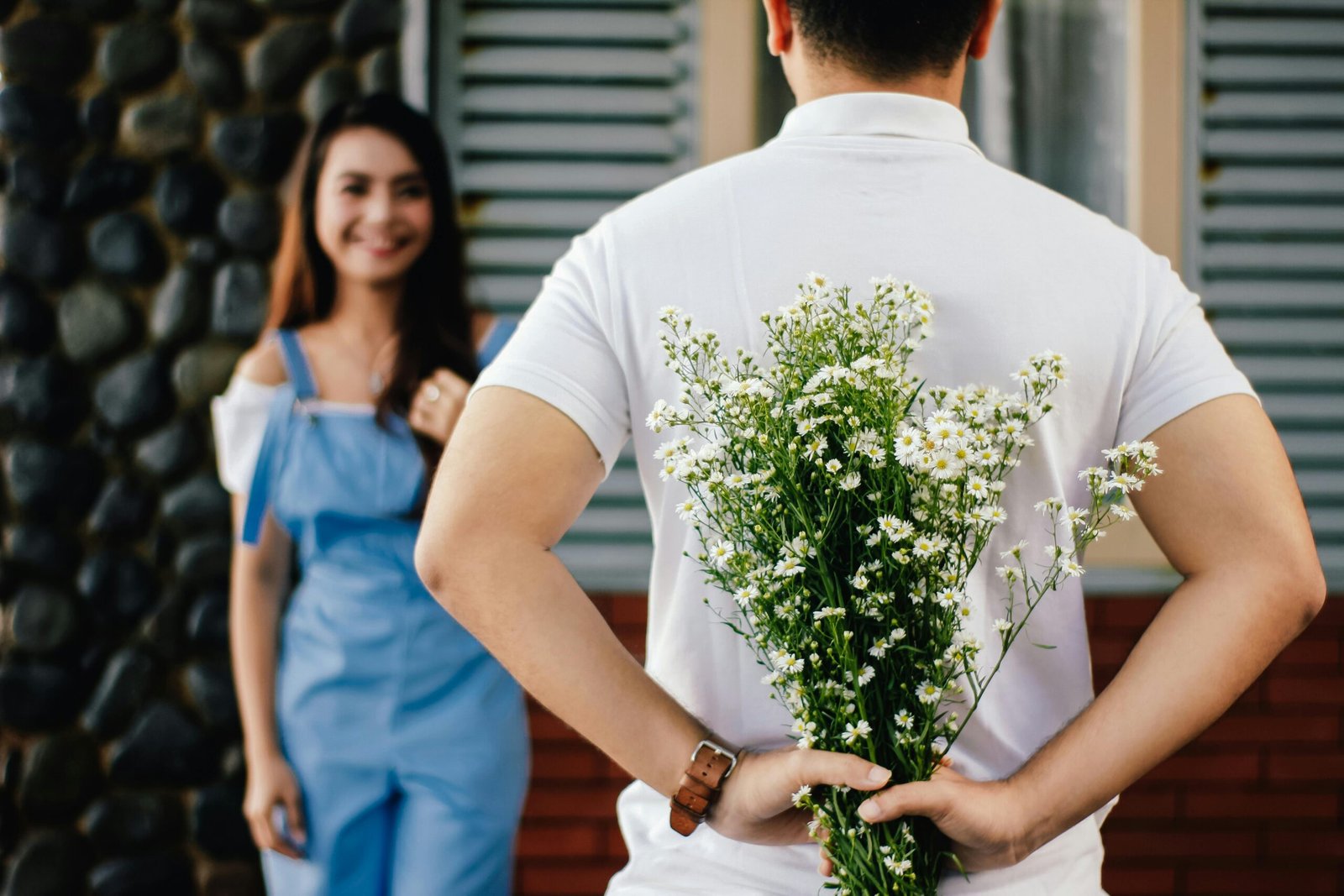 Man hiding flowers behind back, surprising woman happily – Duo Desire dating tip.