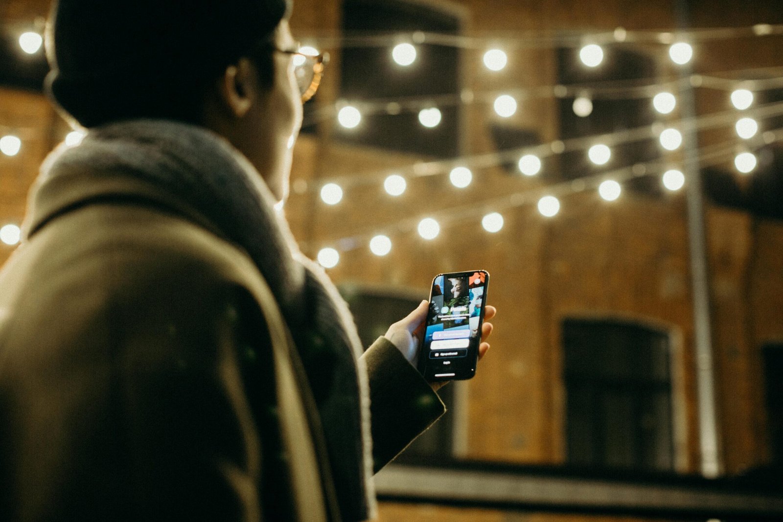 Person using dating app under string lights, browsing Duo Desire for love.