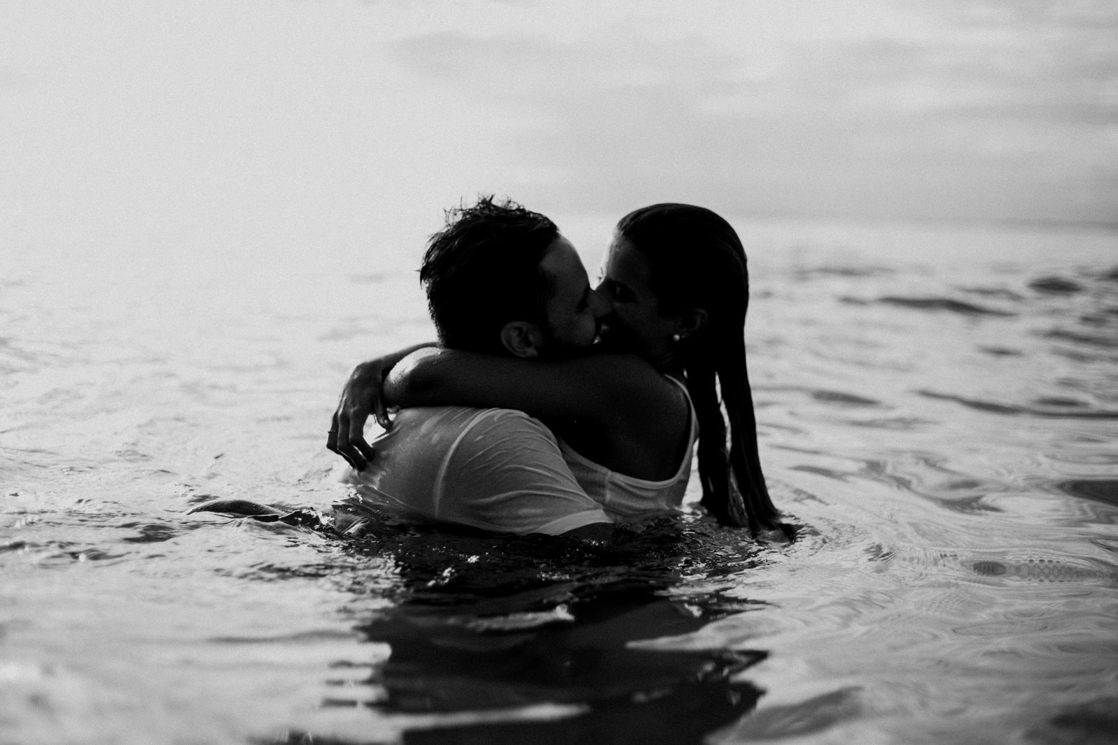 Couple kissing in ocean water during sunset – Duo Desire romantic moment.