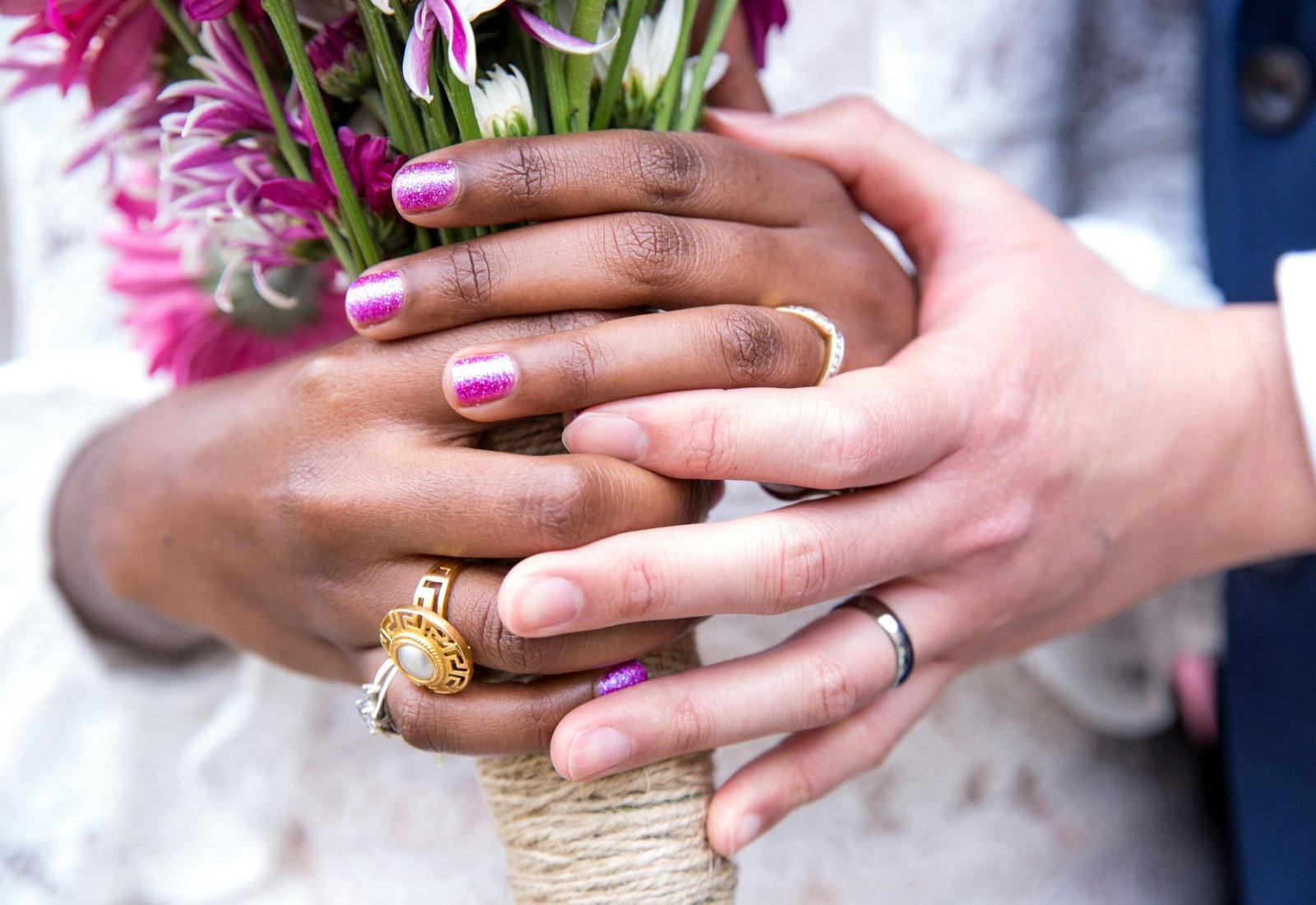 Interracial couple holding hands with wedding rings and flowers – Duo Desire moment.