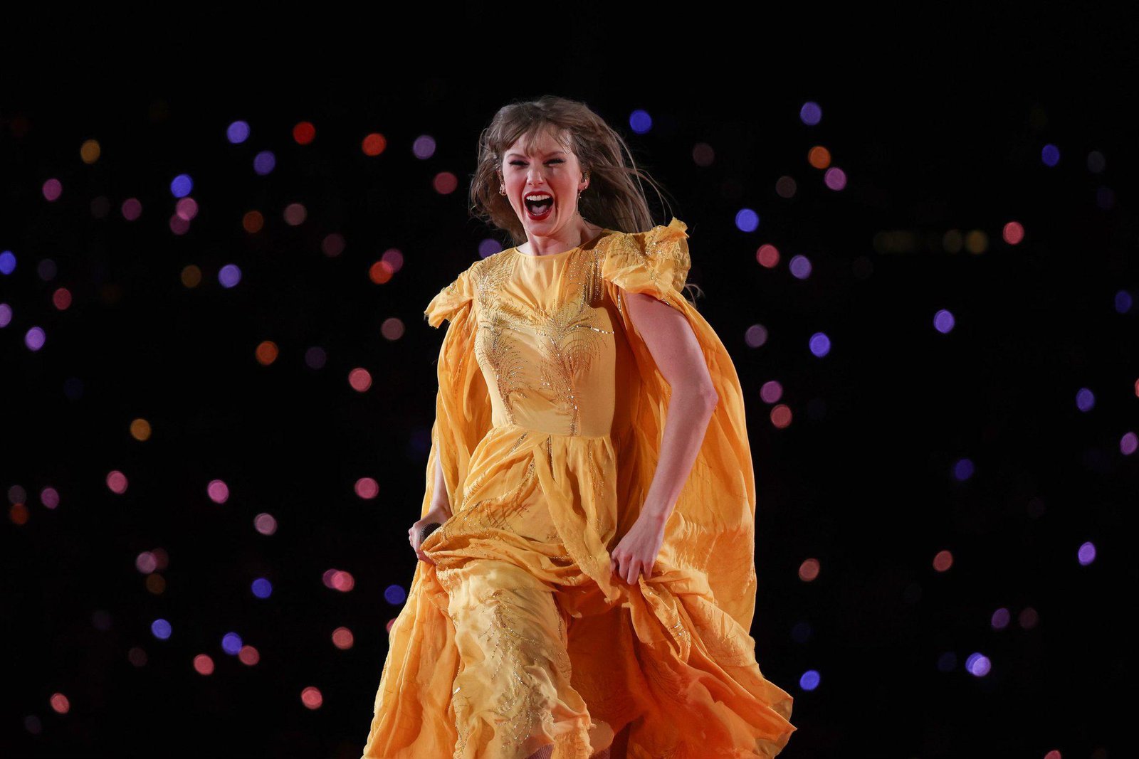 Taylor Swift performs in yellow dress, smiling bright – Duo Desire romance energy.